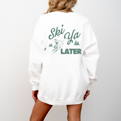 Model wearing a lightweight cotton crewneck sweatshirt with a 'Ski Ya Later' design. The back of the sweatshirt features a vintage boho illustration of a woman skier, adding retro charm to the relaxed, casual fit.