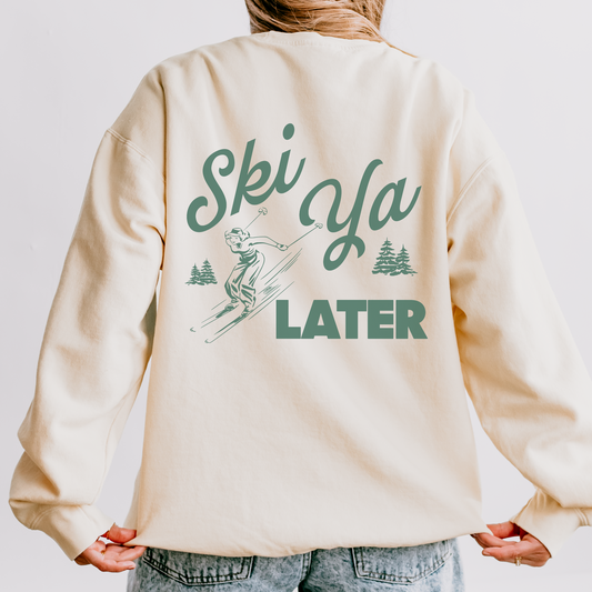 Model wearing a lightweight cotton crewneck sweatshirt with a 'Ski Ya Later' design. The back of the sweatshirt features a vintage boho illustration of a woman skier, adding retro charm to the relaxed, casual fit.