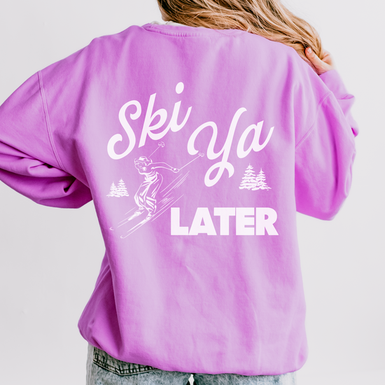Model wearing a lightweight cotton crewneck sweatshirt with a 'Ski Ya Later' design. The back of the sweatshirt features a vintage boho illustration of a woman skier, adding retro charm to the relaxed, casual fit.