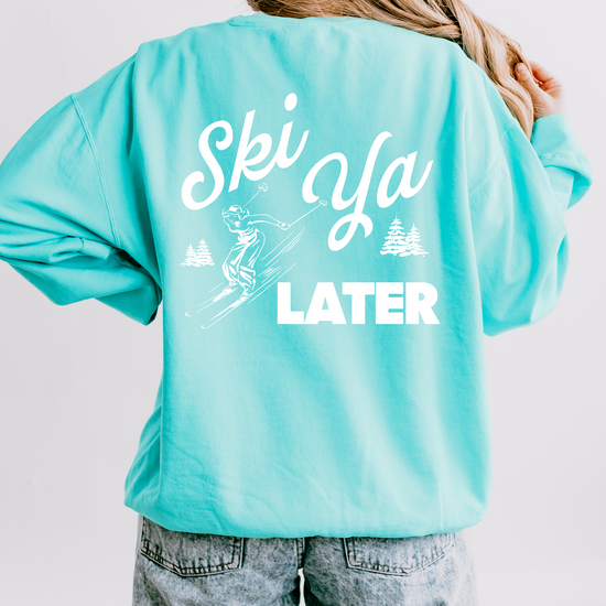 Model wearing a lightweight cotton crewneck sweatshirt with a 'Ski Ya Later' design. The back of the sweatshirt features a vintage boho illustration of a woman skier, adding retro charm to the relaxed, casual fit.