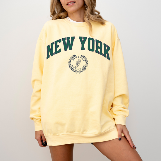A Comfort Colors lightweight cotton crewneck sweatshirt with "New York Track & Field" printed in vintage retro style, giving a refined old money look.